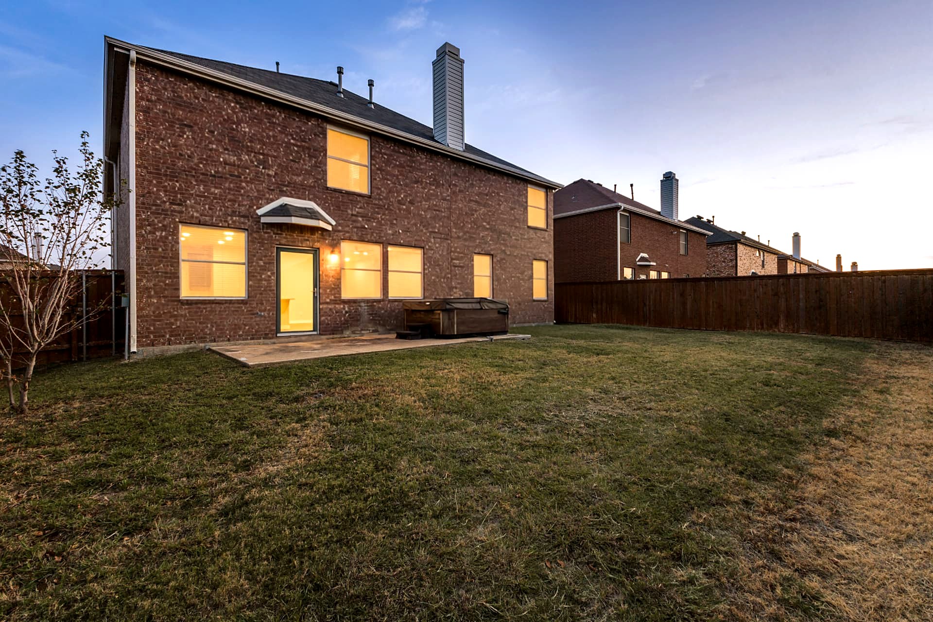 Backyard of 4215 Maidstone Drive at dusk, showing the covered patio, fenced yard and mature trees.