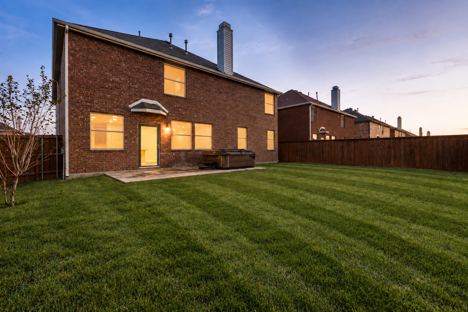 Backyard of 4215 Maidstone Drive at dusk, showing the covered patio, fenced yard and mature trees.